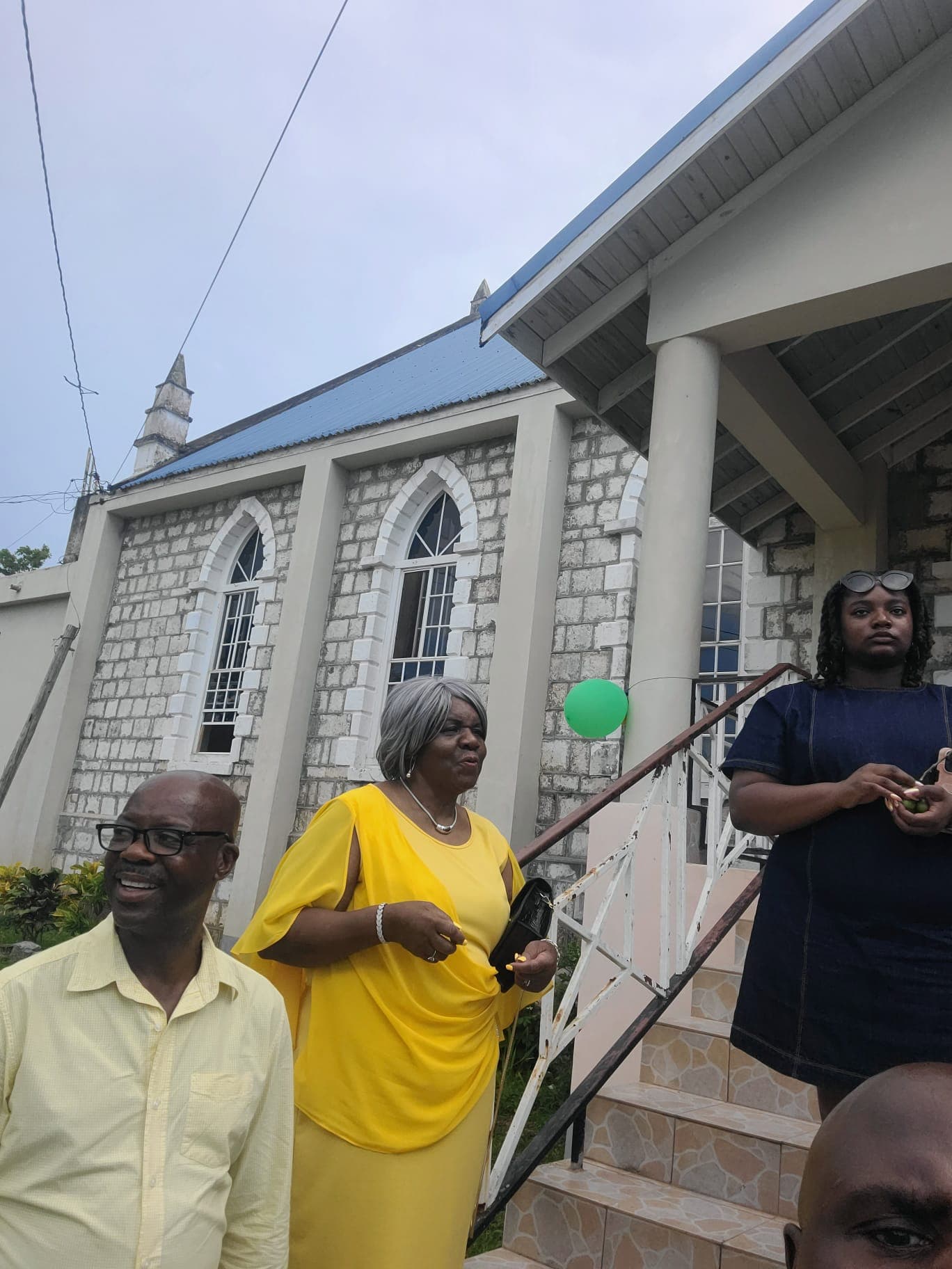 Organizers outside the stone church venue on distribution day, including a woman in a yellow dress greeting arrivals